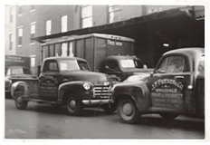 Two early 1920's Feeser's delivery trucks parked in the street facing one another.