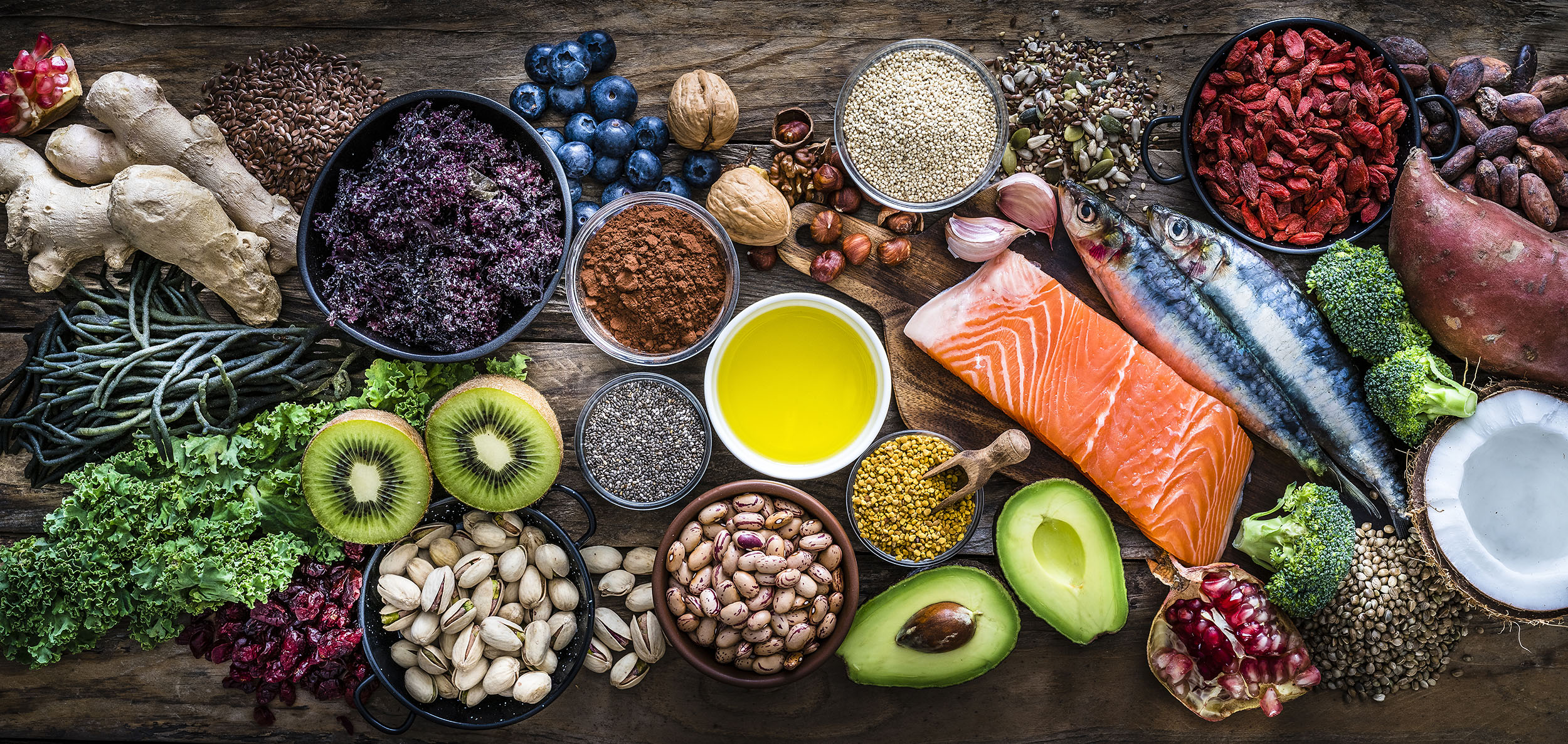 a wooden table topped with bowls of fruits, vegetables, nuts, and raw fish