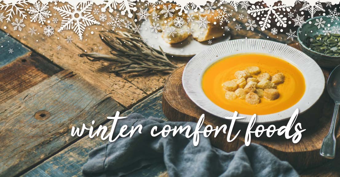 a bowl of soup with croutons resting on a table with slices of bread and fresh herbs