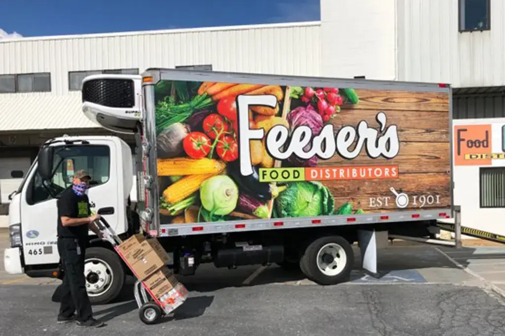 a man using a dolly to load boxes into a branded Feeser's Food Distributors box truck