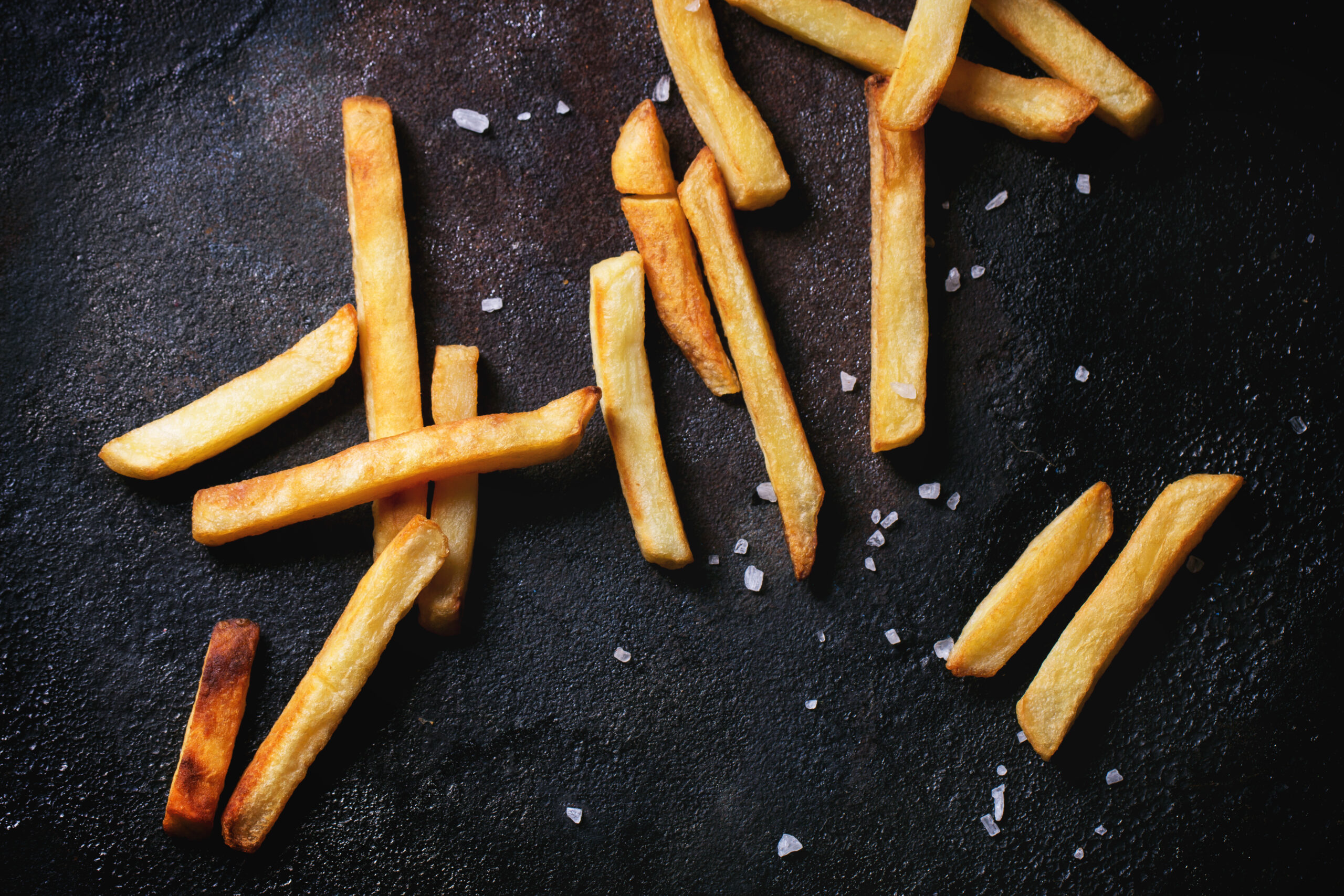 french fries on a black surface with sea salt