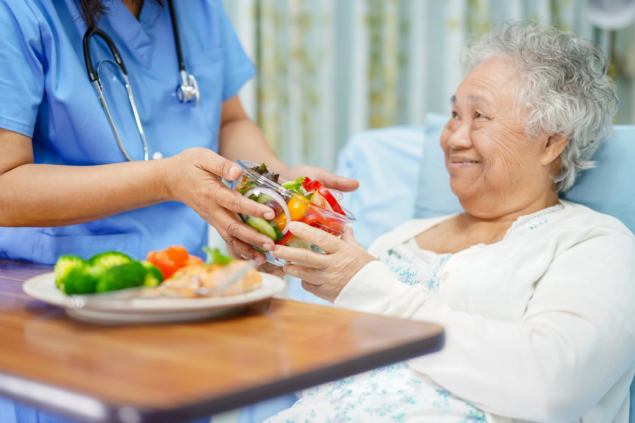 a nurse giving a smiling elderly woman a bowl of vegetables