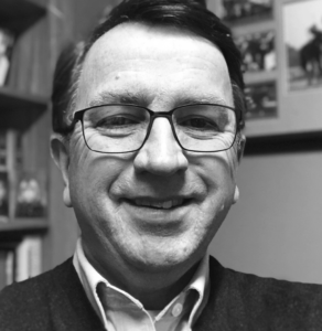 dan spence wearing glasses is smiling in a black and white photo