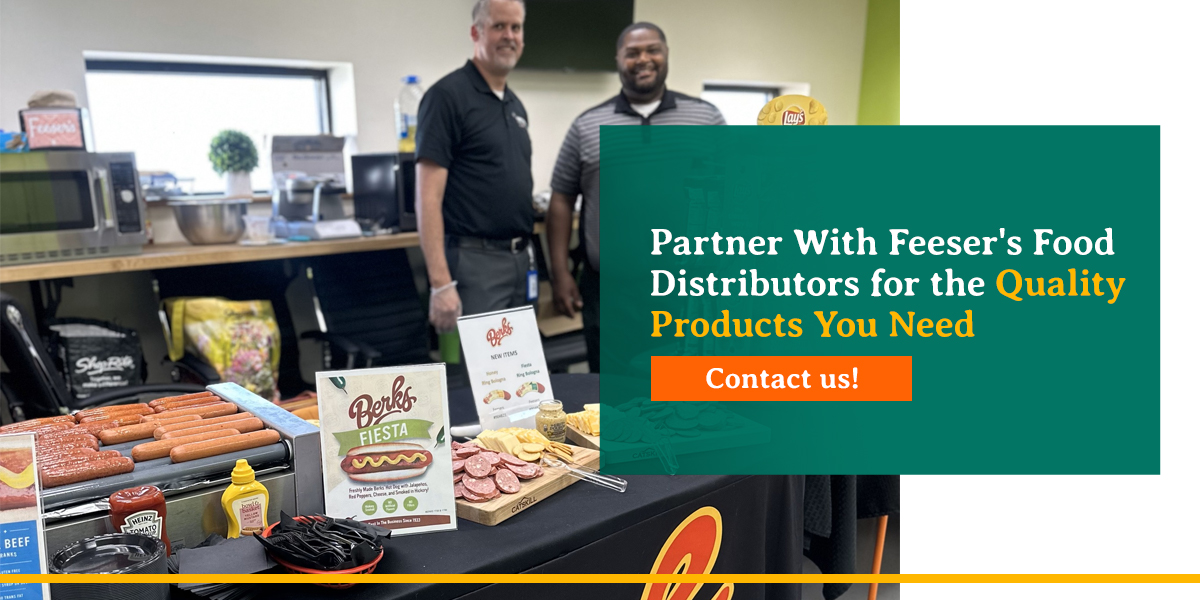 two men standing next to a table of hotdogs with graphic promoting feeser food distributor