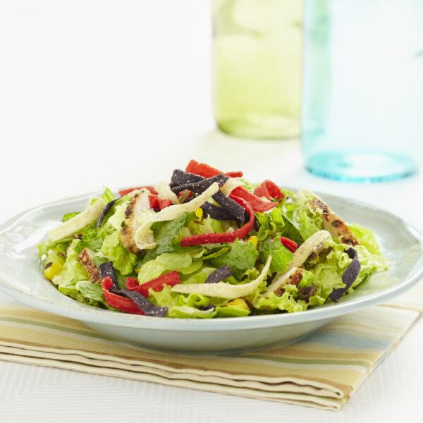 A grilled chicken salad with tortilla strips on it